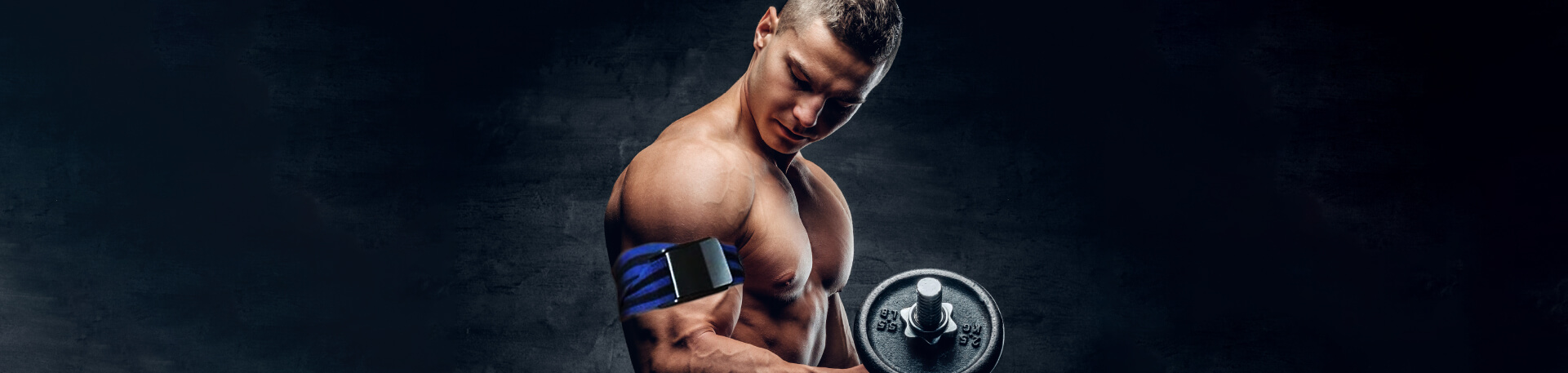 Homem musculado sem camisola a segurar um haltere com o braço direito, usando uma braçadeira de oclusão no braço, num ambiente escuro com fundo neutro.