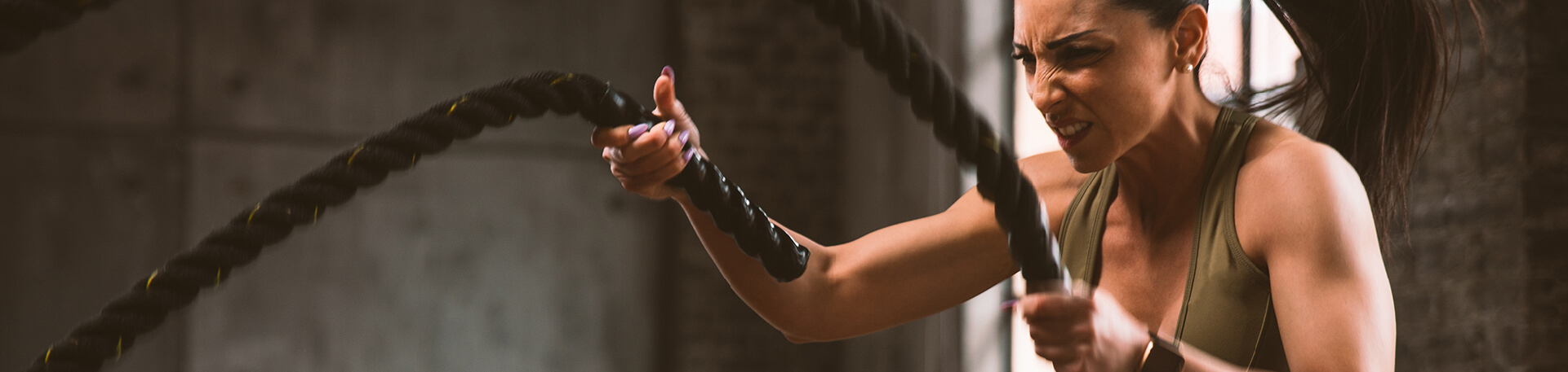 Mulher em treino funcional com cordas de resistência, demonstrando intensidade, força e foco num ambiente de ginásio industrial.