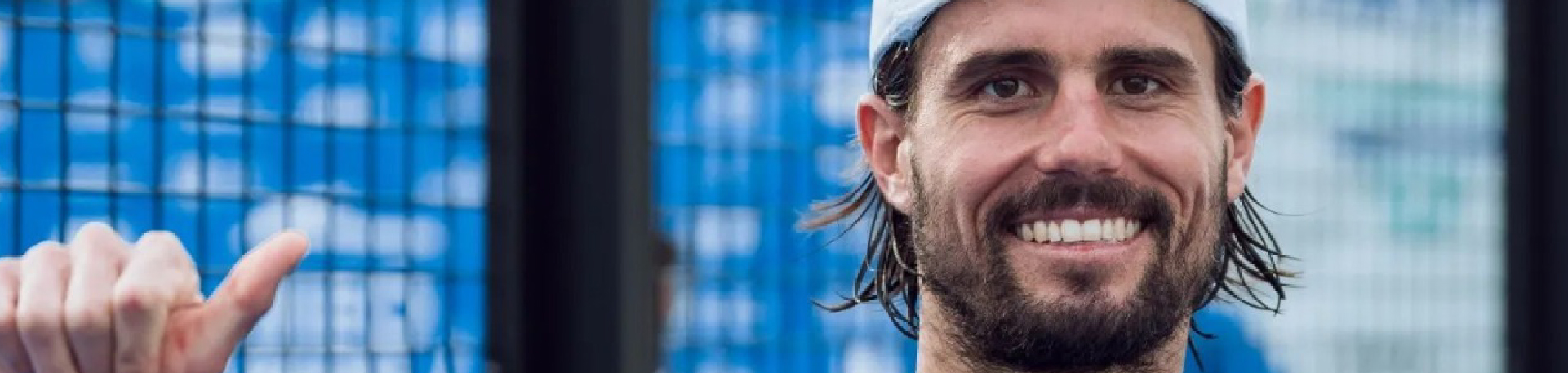 Jogador de padel sorridente com raquete na mão, em campo exterior.