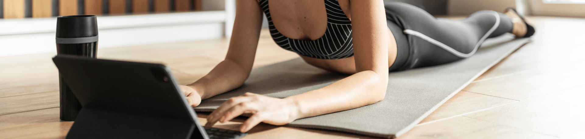 Mulher em roupa de treino a utilizar tablet sobre colchão de exercício.
