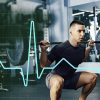 Homem a realizar agachamento com barra carregada no ginásio, com sobreposição de um gráfico de linha estilo eletrocardiograma.