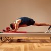 Homem a praticar pilates no equipamento reformer, demonstrando força, controlo e flexibilidade numa sessão de exercício focada no equilíbrio postural e bem-estar físico.