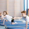 Crianças a praticar exercícios de equilíbrio e coordenação em tapetes de ginástica, promovendo o desenvolvimento motor e hábitos saudáveis através da actividade física.