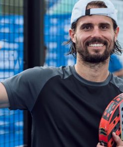 Jogador de padel sorridente com raquete na mão, em campo exterior.