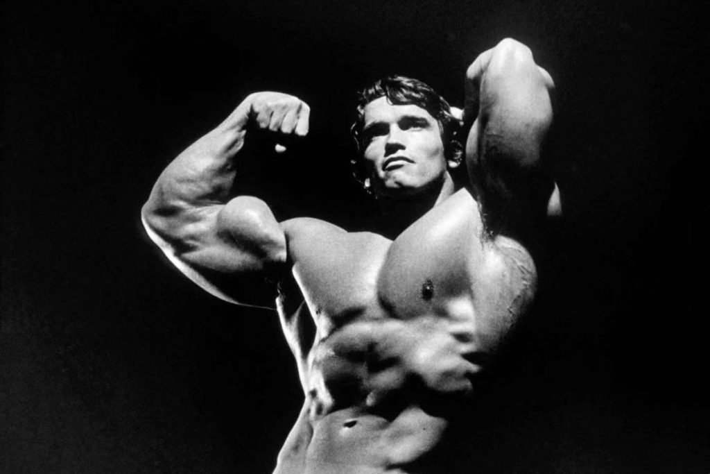 Arnold Schwarzenegger em pose icónica de culturismo, símbolo de disciplina, superação e motivação no desporto de alta performance.